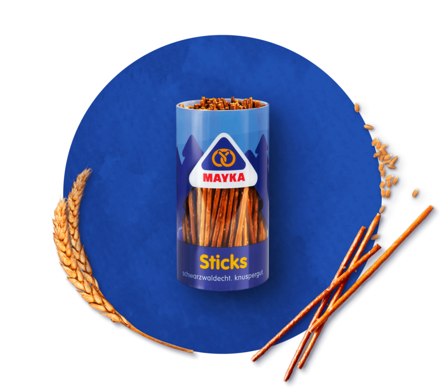 MAYKA Bio Sticks und Mini-Brezeln in Runddosen eingerahmt von Weizenähren und Weizenkörnern und einzelnen Salzstangen und Brezeln auf grünem Hintergrund
